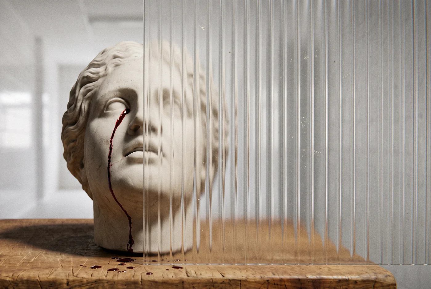 Marble head on a butcher's block behind ribbed glass, a tear of blood and a few drops